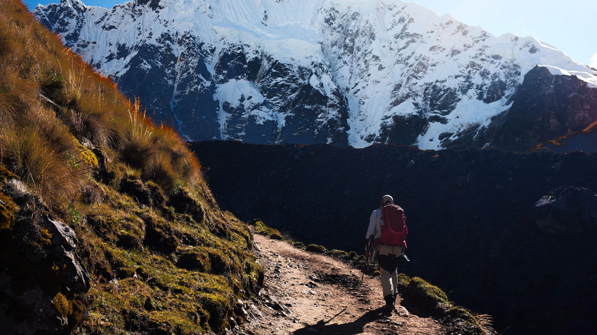 Trekker with red backpack hiking through the Andes toward snow-covered mountains, illustrating the Salkantay Trek Packing List essentials – Magical Cusco Travel Agency