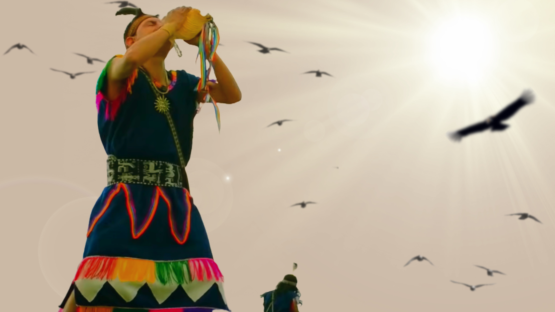 Participant in vibrant Andean attire holds a ceremonial object adorned with ribbons, representing Inti Raymi instruments under a radiant sky – Magical Cusco Travel Agency