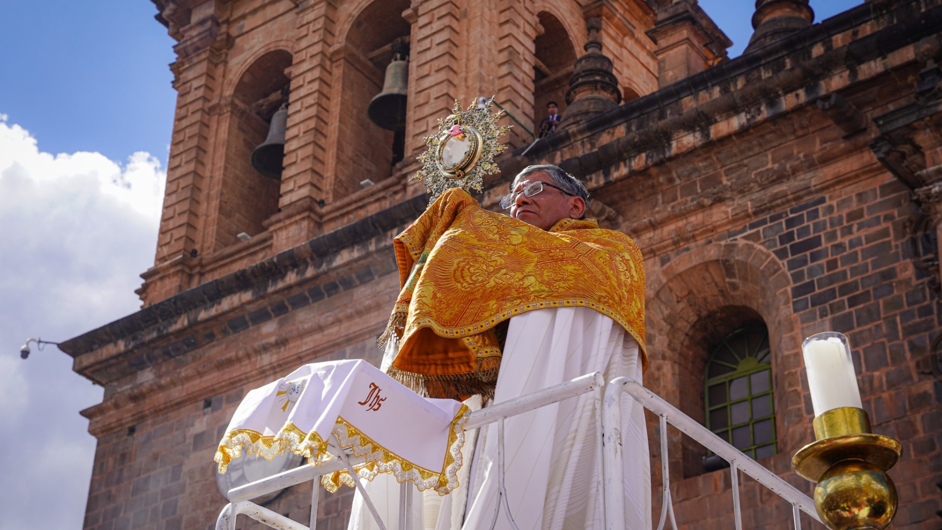 A priest holding an ornate monstrance during the solemn Corpus Christi mass in Cusco, with the ancient cathedral bells visible in the background - Magical Cusco Travel Agency.