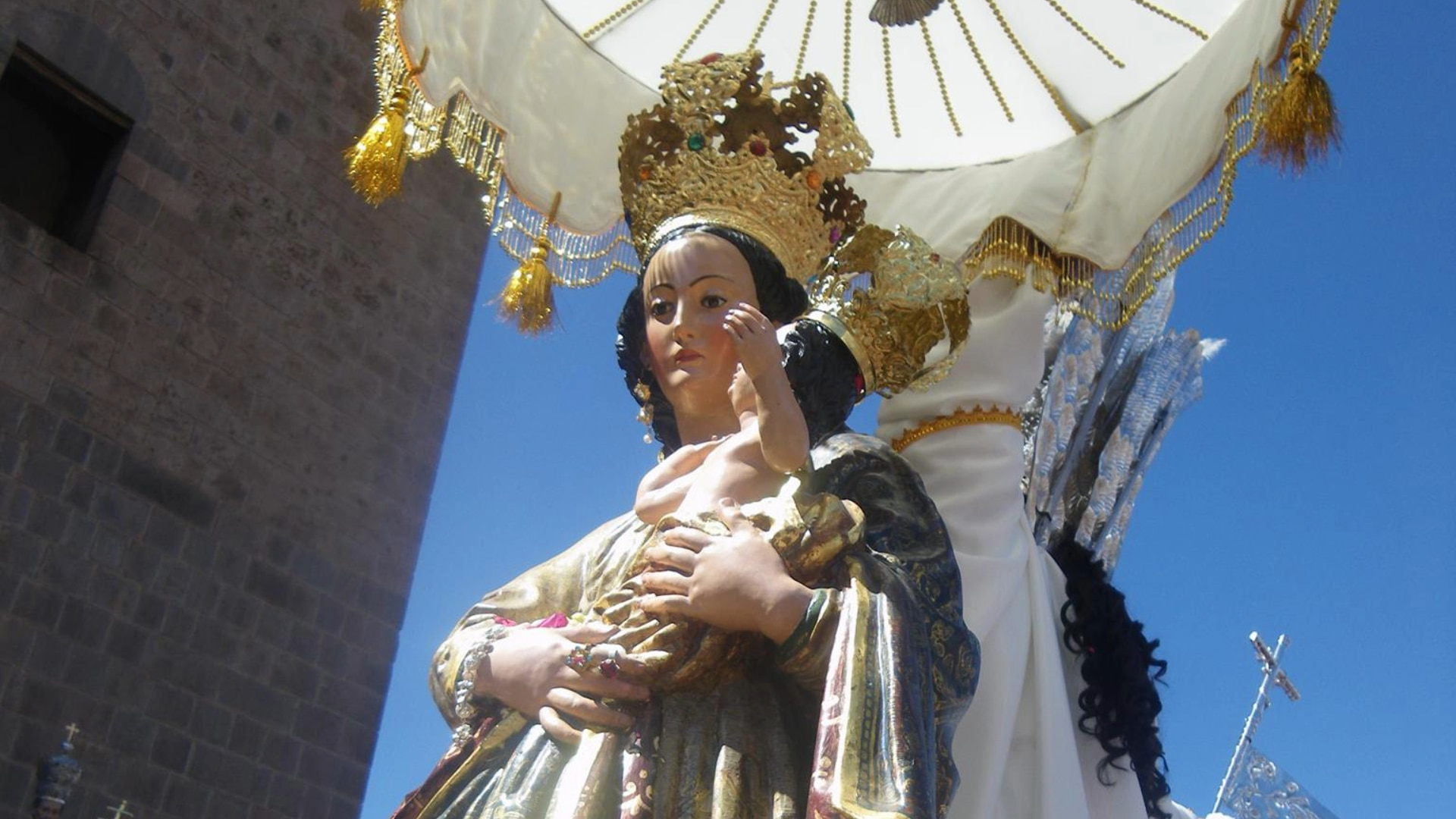 Close-up of a religious statue of the Virgin Mary holding baby Jesus, adorned with crowns and ornate vestments, being carried during a traditional procession in Cusco - Magical Cusco Travel Agency.