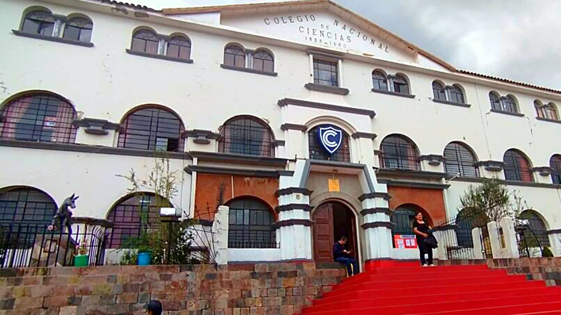 A front view of the imposing facade of the Colegio Nacional de Ciencias in Cusco, a historic building with a large red staircase. - Magical Cusco Travel Agency