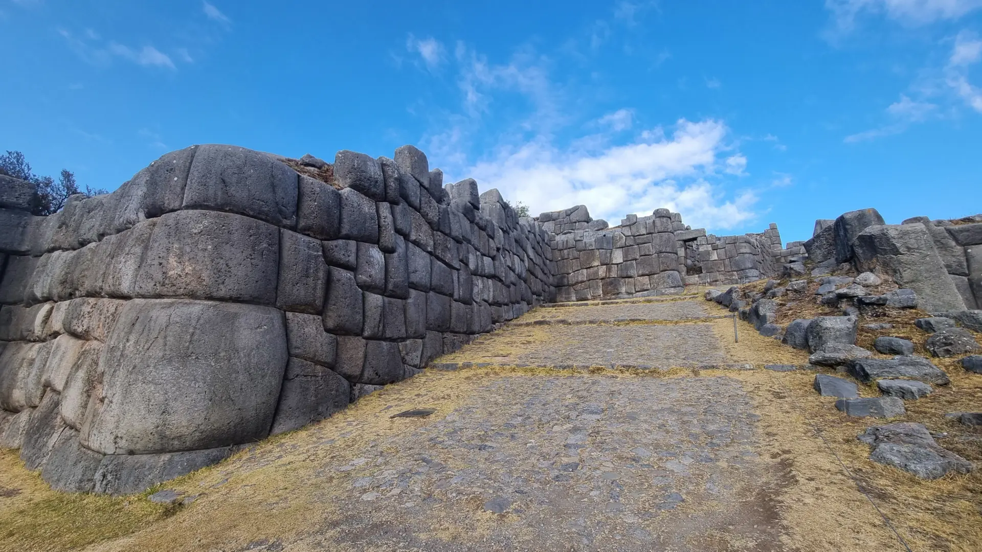 Imposing Inca stone wall with a staircase, showing the magnificent engineering and design of the Sacsayhuamán fortress under a clear sky. - Magical Cusco Travel Agency