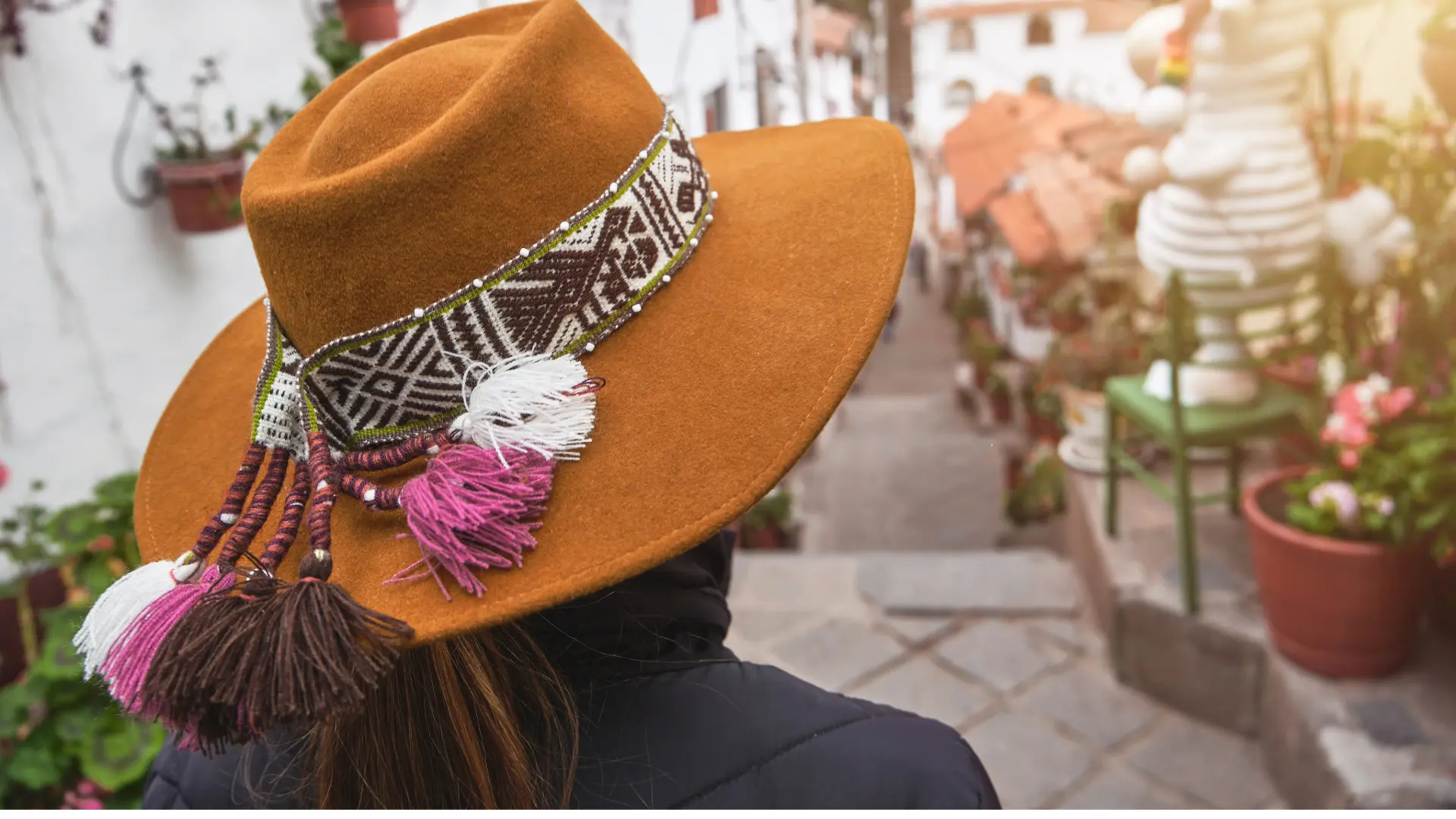 View from behind of a traveler wearing a traditional Andean hat decorated with tassels, looking down a street in Cusco, ready for a day of Walking Cusco. - Magical Cusco Travel Agency