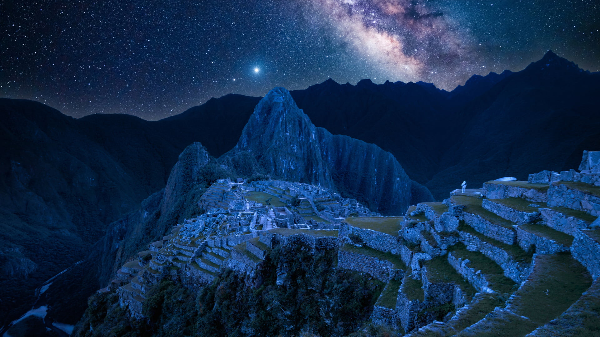 Bluish-lit stone ruins of Machu Picchu beneath a star-filled sky and the Milky Way, with Huayna Picchu rising in the background—capturing the cosmic harmony and ancestral wisdom of Ancient Astronomy in Andean Communities – Magical Cusco Travel Agency
