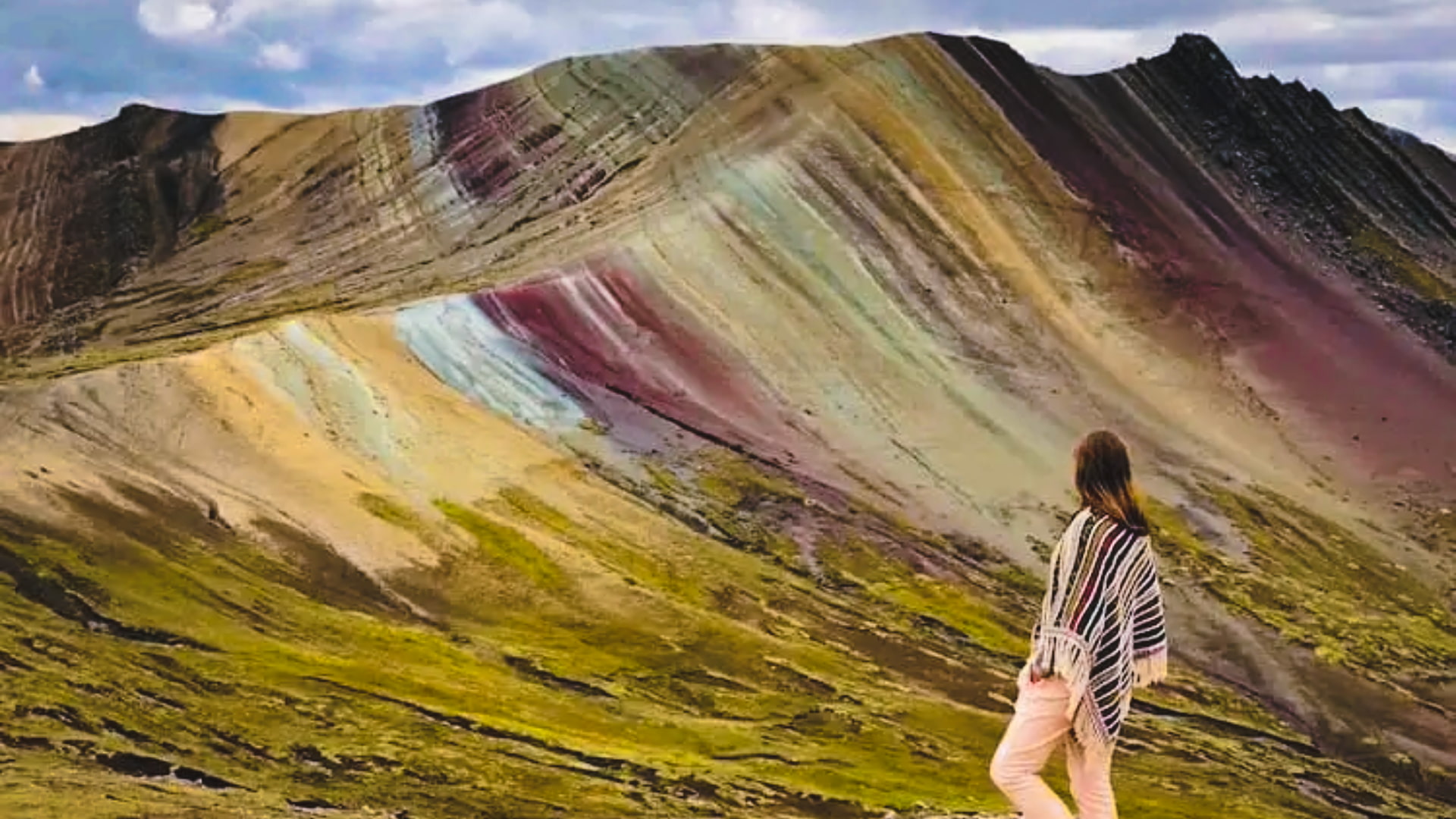 Female traveler in striped poncho standing before the vibrant mineral layers of Palccoyo Rainbow Mountain – Magical Cusco Travel Agency